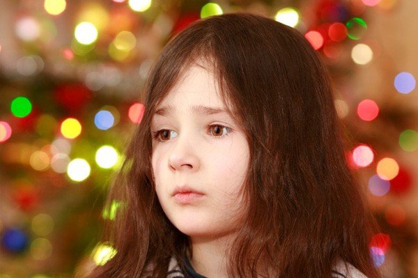 Child looking warily standing in front of a christmas tree