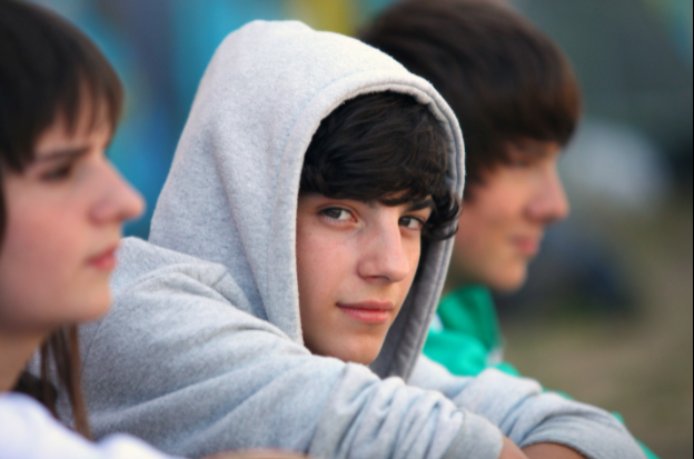 Boy in gray hoodie looking at camera and sitting between two other teens